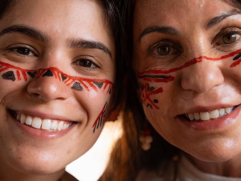 Duas visitantes sorrindo com pintura facial indígena durante o Day Tour Fluvial