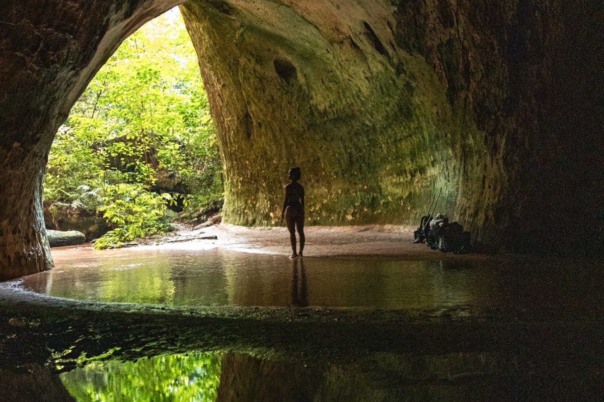 Silhueta de visitante na entrada de uma gruta com reflexo na água parada